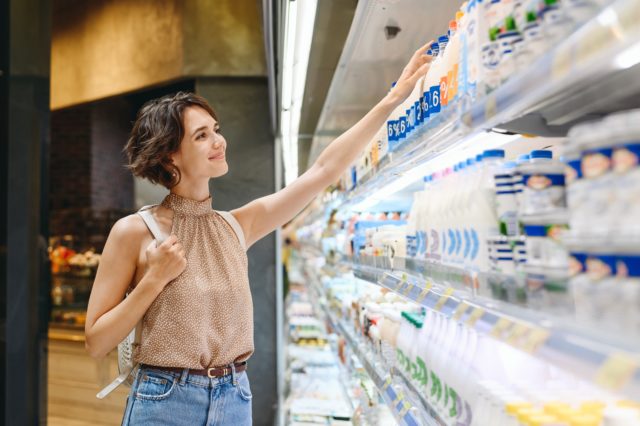 Pessoa dentro de um supermercado na área de frios, escolhendo um produto e com uma expressão feliz.
